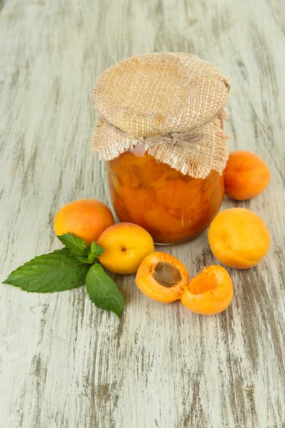 Apricot jam in glass jar and fresh apricots, on wooden background — Stock Photo, Image