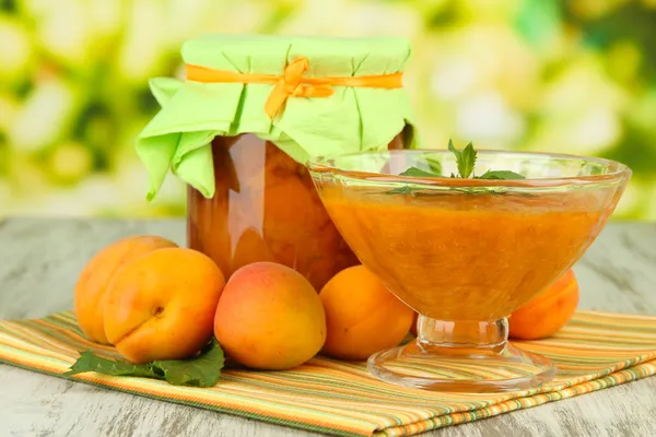 Confiture d'abricots dans un bocal en verre et abricots frais, sur table en bois, sur fond lumineux — Photo