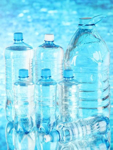 Agua en diferentes botellas sobre fondo azul —  Fotos de Stock