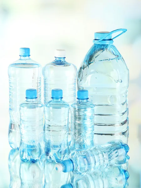 Water in different bottles on light background — Stock Photo, Image