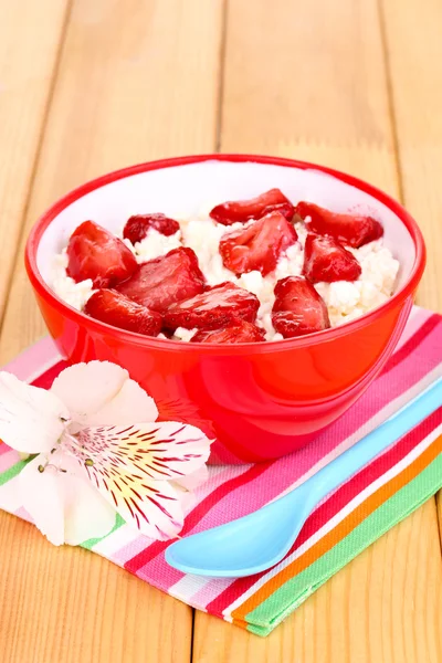 Hüttenkäse in roter Schüssel mit Erdbeeren in Scheiben auf Holztisch — Stockfoto