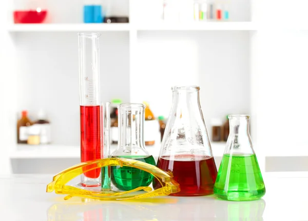 Verschillende laboratoriumglaswerk met kleur vloeistof op laboratorium achtergrond — Stockfoto