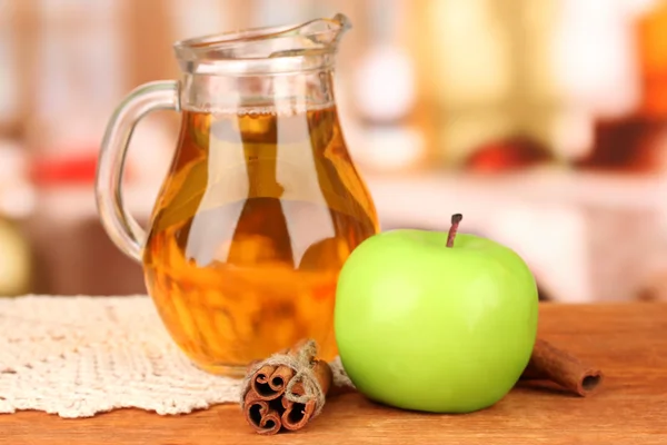 Jarra llena de zumo de manzana y manzana sobre mesa de madera sobre fondo brillante — Foto de Stock