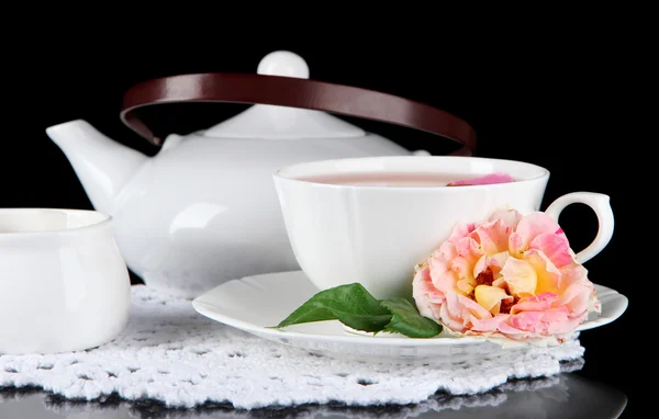 Wasserkocher und Tasse Tee aus Teerose auf Serviette schwarzer Hintergrund — Stockfoto