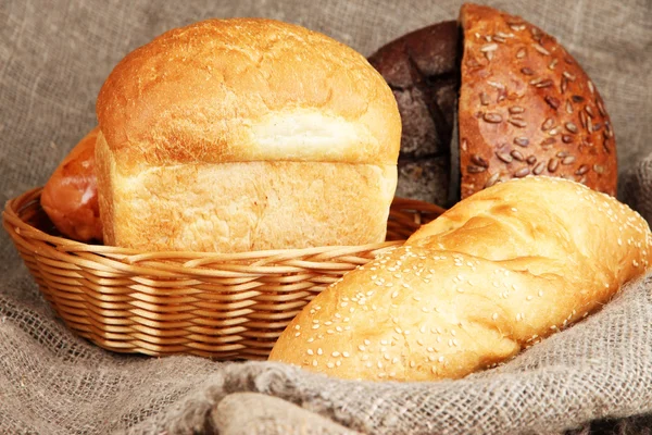 Baked bread in wicker basket on burlap background — Stock Photo, Image