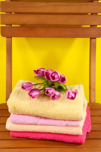 Handtücher und Blumen auf Holzstuhl auf gelbem Hintergrund — Stockfoto