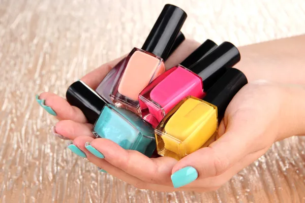 Beautiful woman hands with blue manicure and several bottles with nail polish, on color background — Stock Photo, Image
