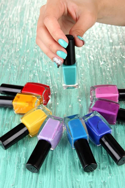 Beautiful woman hands with blue manicure and several bottles with nail polish, on color background — Stock Photo, Image