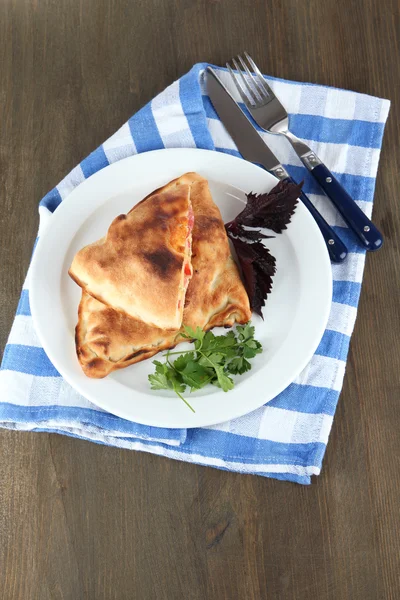 Pizza calzones on plate on napkin on wooden table — Stock Photo, Image