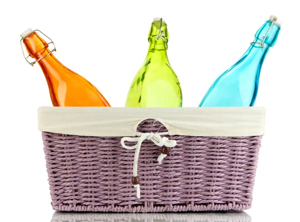 Botellas de vidrio de color en canasta de mimbre, aisladas en blanco — Foto de Stock
