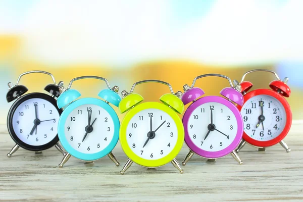 Relógios de alarme coloridos na mesa em fundo brilhante — Fotografia de Stock