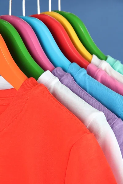 Verschillende shirts op kleurrijke hangers op blauwe achtergrond — Stockfoto