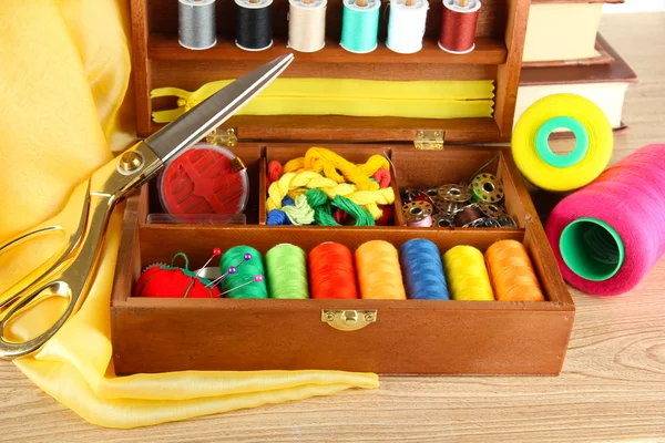 Sewing kit in wooden box with books and cloth table on bright background