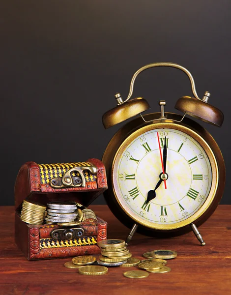Antyczny zegar i monety na drewnianym stole na czarnym tle — Zdjęcie stockowe