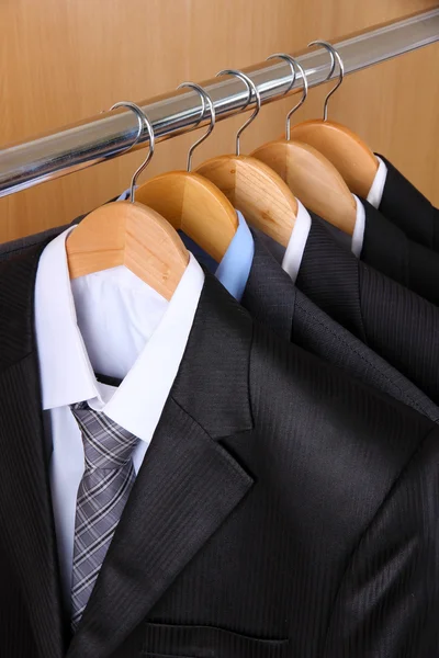 Anzüge mit Hemden auf Kleiderbügeln auf hölzernem Hintergrund — Stockfoto