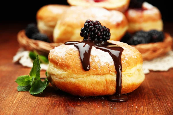 Donuts saborosos com chocolate e bagas na mesa de madeira — Fotografia de Stock
