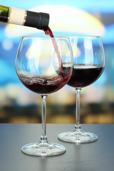 Vinho tinto sendo derramado em copo de vinho, em fundo brilhante — Fotografia de Stock