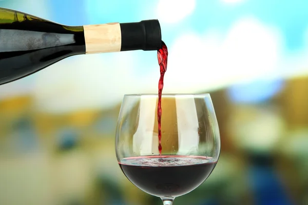Červené víno se nalije do sklenice na víno, na světlé pozadí — Stock fotografie