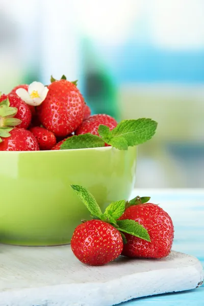 Zralé sladké jahody v zelené prohlubni na modré dřevěný stůl — Stock fotografie