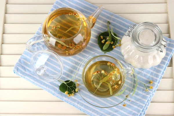 Hervidor de agua y taza de té con tilo en servilleta sobre mesa de madera —  Fotos de Stock