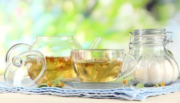 Wasserkocher und Tasse Tee mit Linde auf Serviette auf Holztisch auf Naturhintergrund — Stockfoto