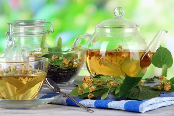 Bollitore e tazza di tè con tiglio sul tavolo di legno sullo sfondo della natura — Foto Stock