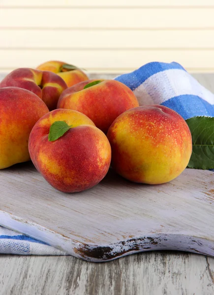 Peaches on board on napkin on table on wooden background — Stock Photo, Image