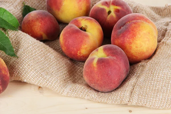 Peaches on sackcloth on wooden table — Stock Photo, Image