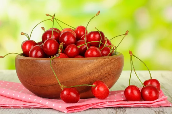 Cherry berries in bowl on wooden table on bright background — Stock Photo, Image