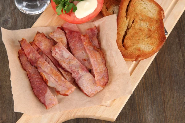 Bacon on plates on board on wooden table — Stock Photo, Image