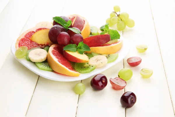 Surtido de frutas en rodajas en plato, sobre mesa de madera blanca — Foto de Stock