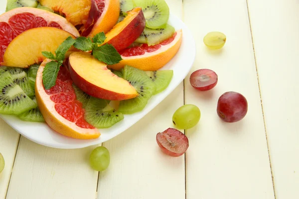 Ассортимент нарезанных фруктов на тарелке, на белом деревянном столе — стоковое фото