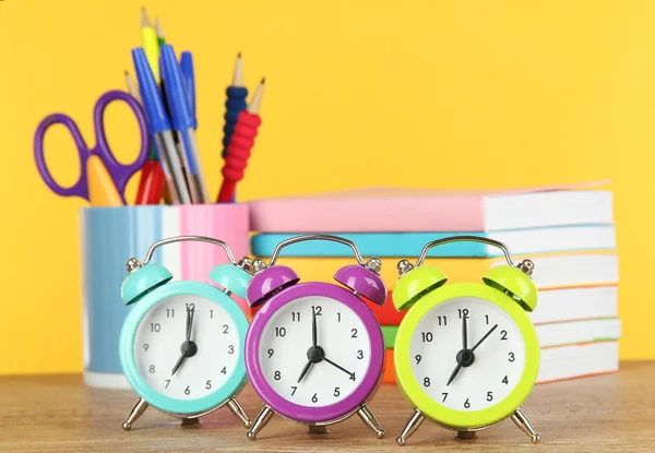 Relógio de alarme colorido na mesa no fundo amarelo — Fotografia de Stock