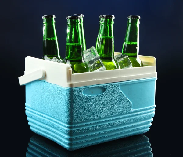 Bottles of beer with ice cubes in mini refrigerator, on dark blue background — Stock Photo, Image