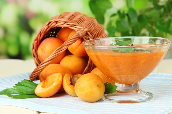 Apricot jam in glass bowl and fresh apricots, on wooden table, on bright background — Stock Photo, Image
