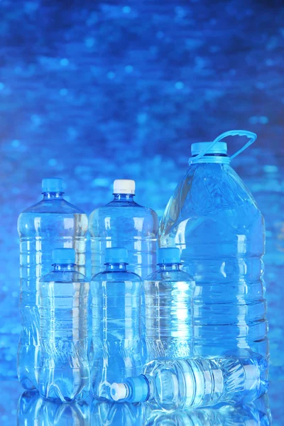 Agua en diferentes botellas sobre fondo azul — Foto de Stock