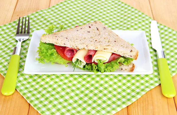 Sandwich savoureux avec saucisse de salami et légumes sur assiette blanche, sur fond de bois — Photo