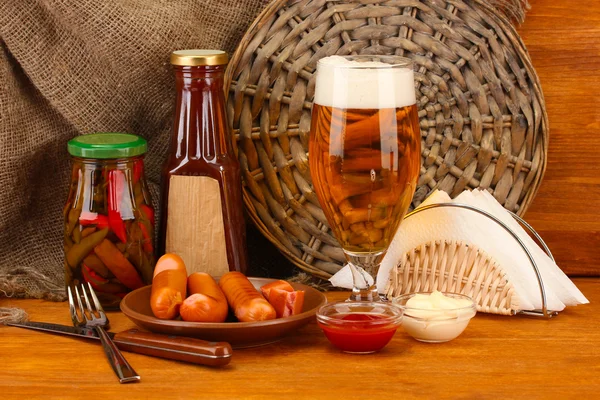 Bière et saucisses grillées sur table en bois sur fond de sac — Photo