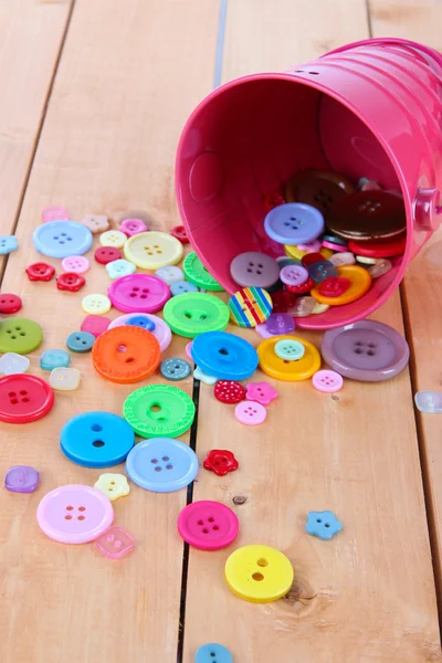 Colorful buttons strewn from bucket on wooden background — Stock Photo, Image