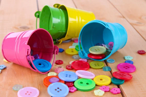 Colorful buttons strewn from buckets on wooden background — Stock Photo, Image