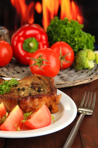 Trozo de carne frita en el plato en la mesa de madera sobre fondo de fuego — Foto de Stock