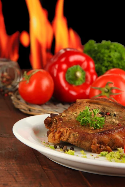 Trozo de carne frita en el plato en la mesa de madera sobre fondo de fuego — Foto de Stock