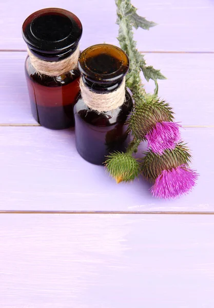 Medicine bottles with thistle flowers on wooden background — Stock Photo, Image