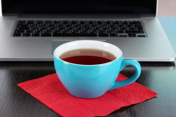 Blue cup on napkin on laptop background on wooden table — Stock Photo, Image
