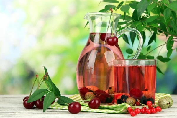 Pitcher and glass of compote with summer berries on natural background — Stock Photo, Image