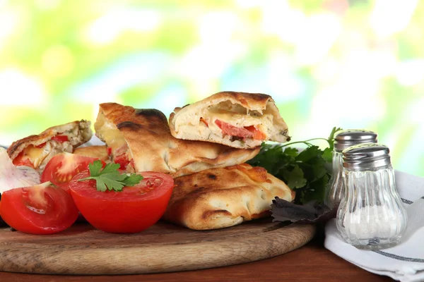 Pizza calzones on wooden board near napkin on wooden table on nature background — Stock Photo, Image