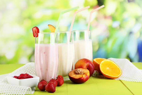 Leckere Milchshakes mit Erdbeeren und Pfirsich auf Holztisch vor natürlichem Hintergrund — Stockfoto