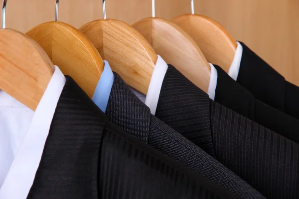 Suits with shirts on hangers on wooden background — Stock Photo, Image