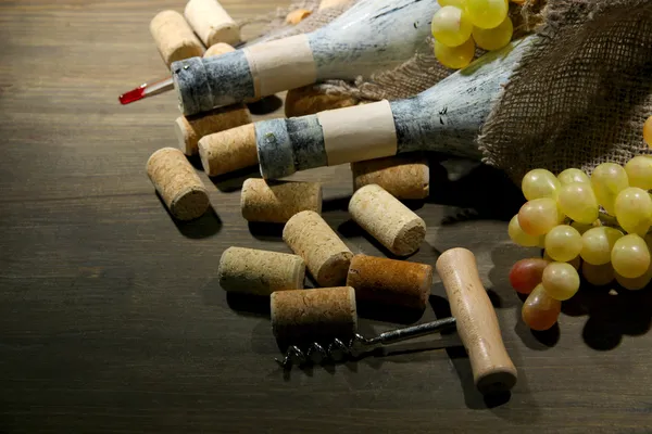 Old bottles of wine, grapes and corks on wooden background — Stock Photo, Image