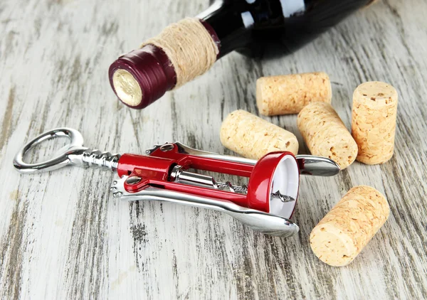 Corkscrew with wine corks and bottle of wine on wooden table close-up — Stock Photo, Image